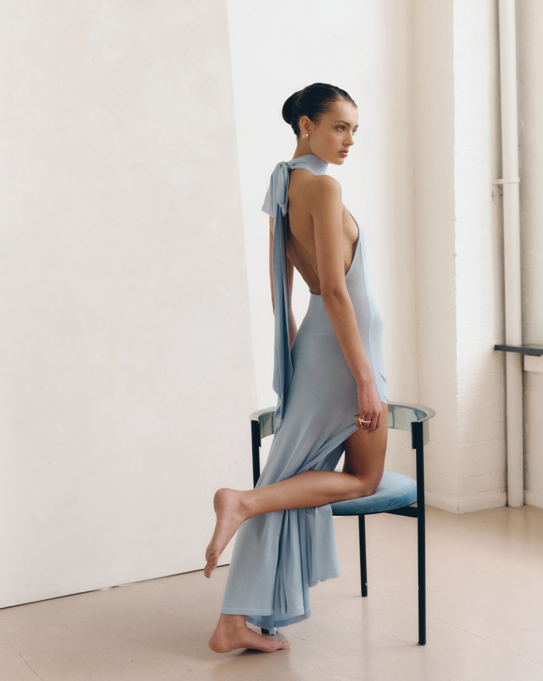 Model wearing the LENY Cascade Dress 2.0 in Aquamarine, styled as an elegant blue backless maxi dress with a halter tie neckline.
